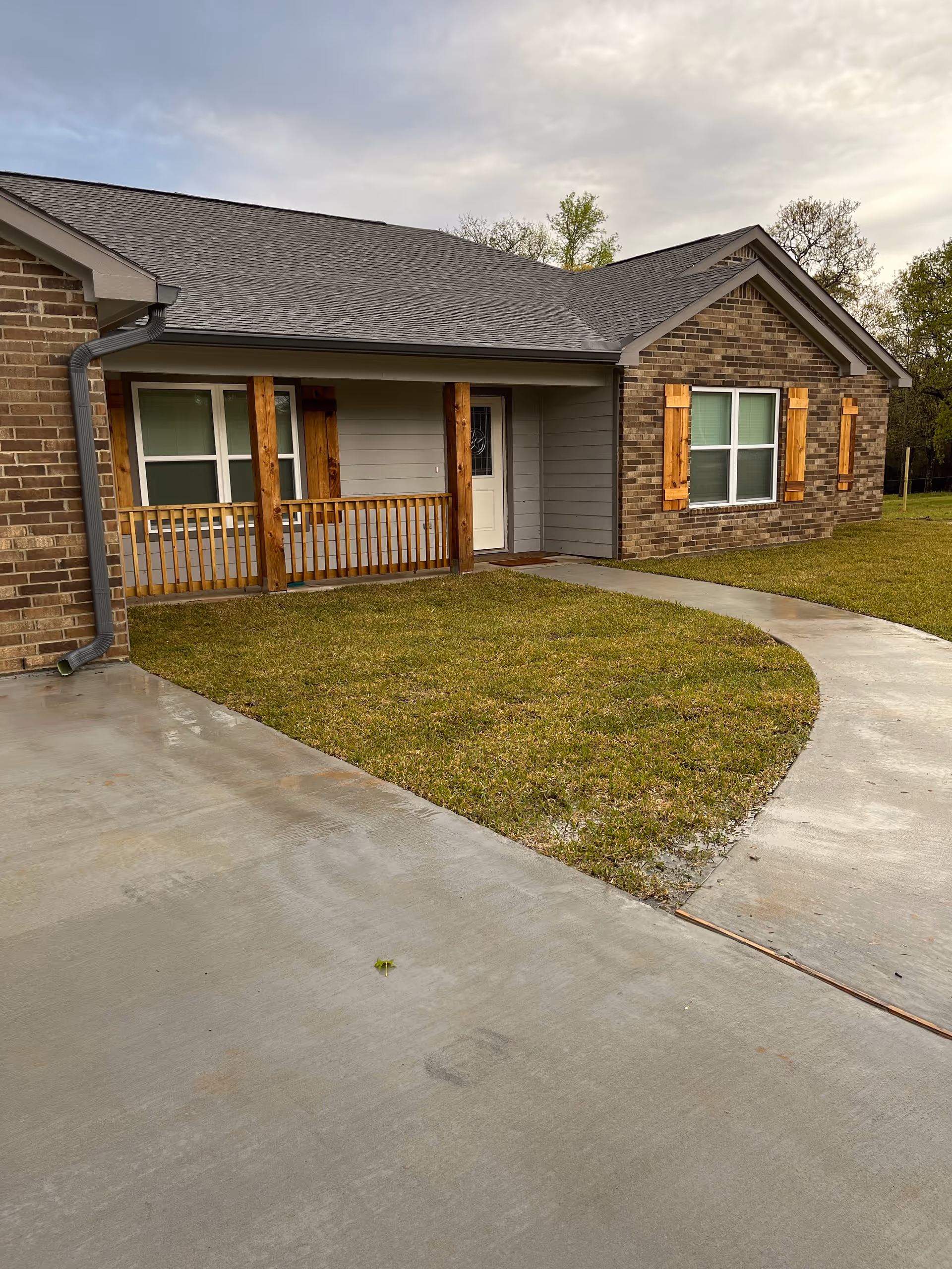 Brick exterior house with a small porch, wooden railing, and curved concrete walkway.