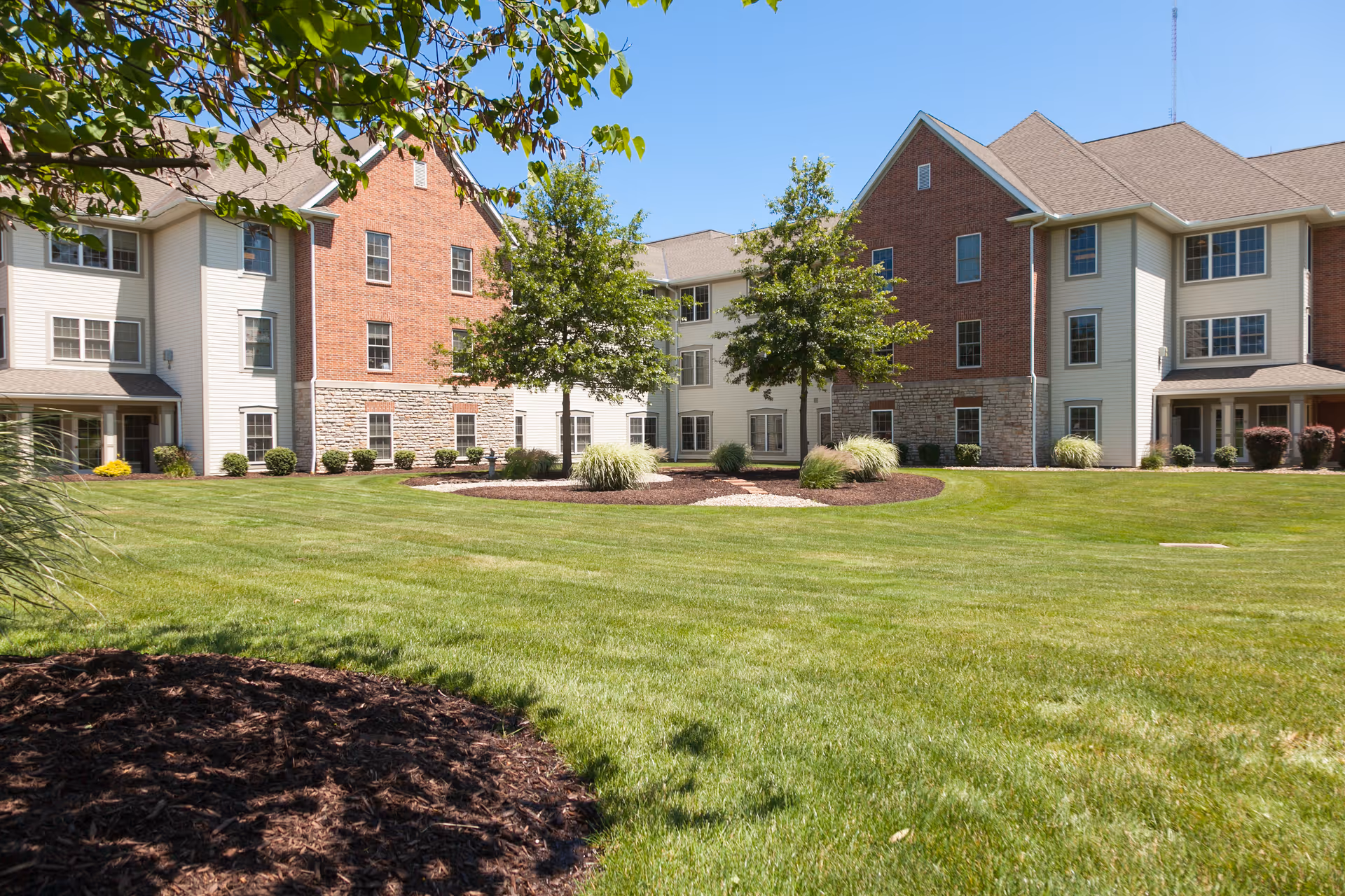 Well-manicured lawn frames a multi-building senior living campus with brick and beige siding.