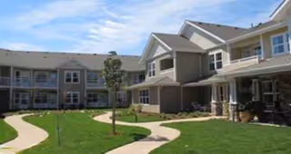 Exterior view of a senior living facility with manicured lawn and curved walkway.