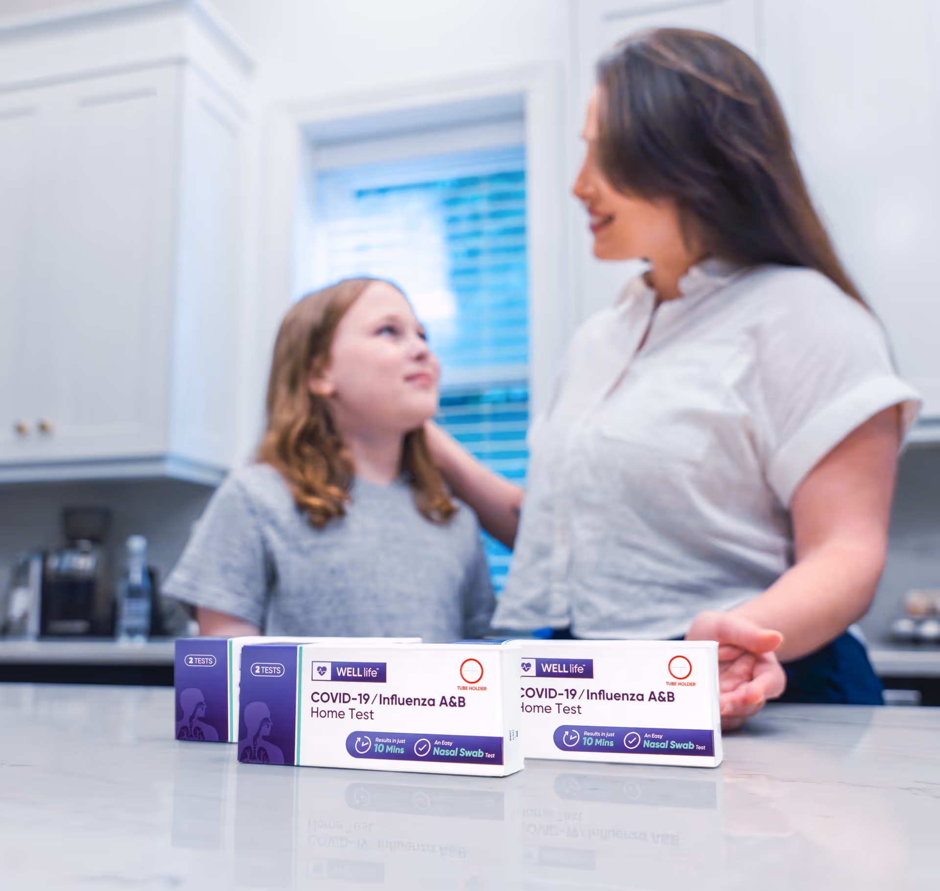 Two people stand in a bright kitchen behind a counter with COVID-19 home test boxes.