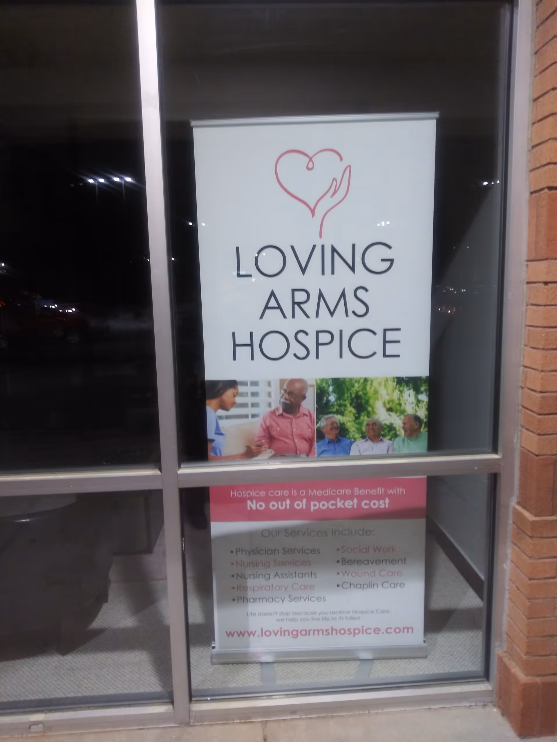 Storefront window displays Loving Arms Hospice sign with heart logo and service photos.