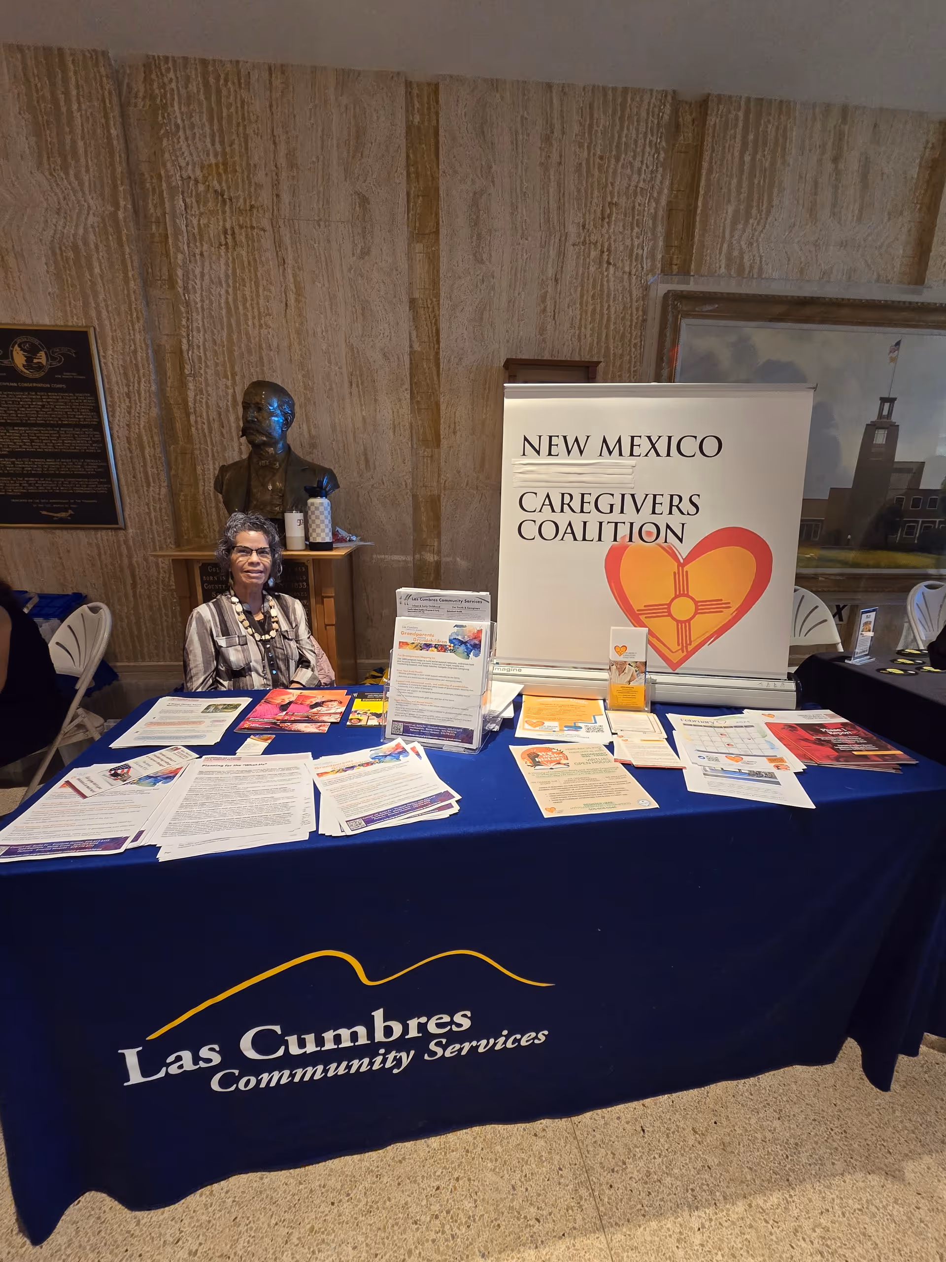 A person sits at a desk with brochures at an indoor community services booth.
