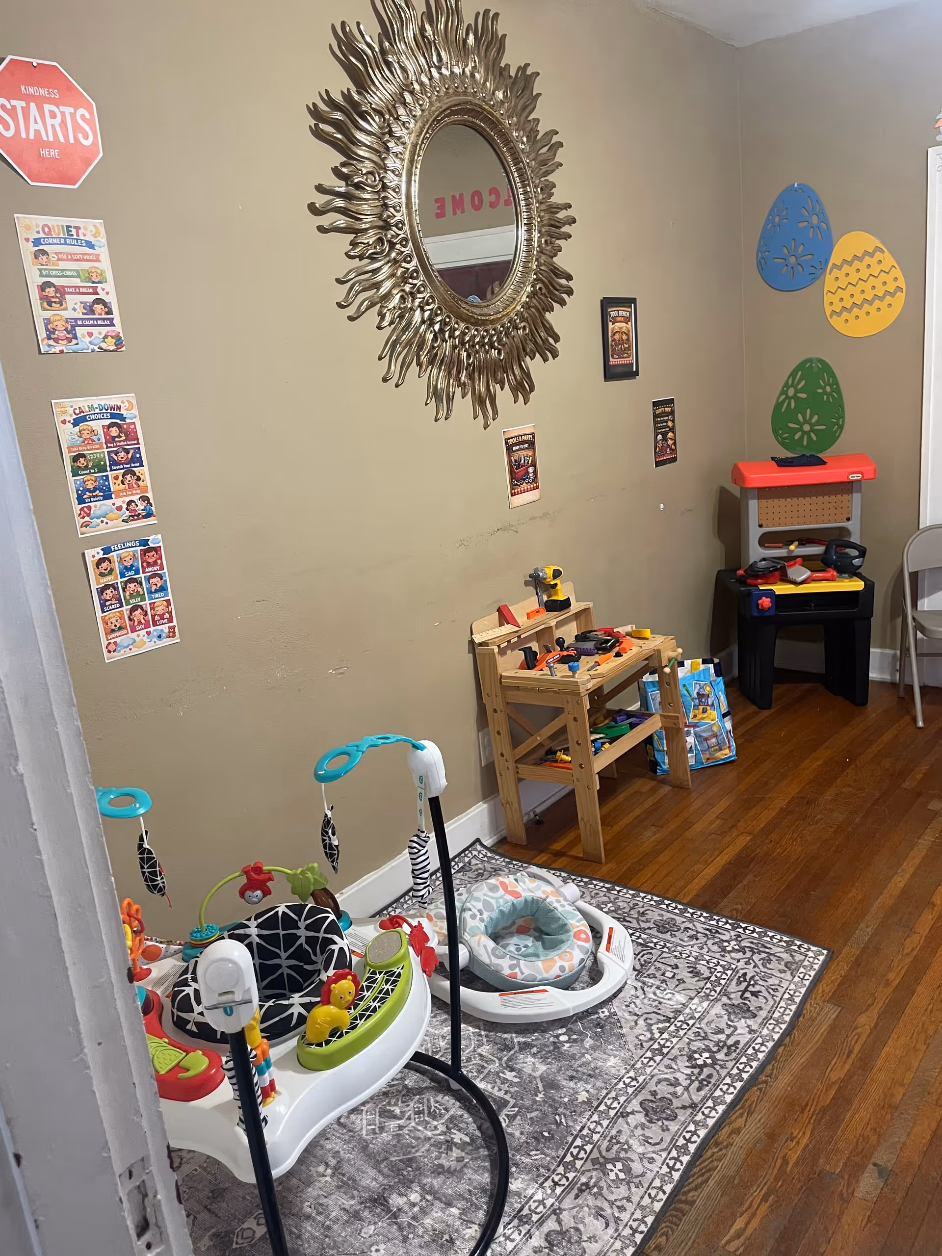 Play area with toys and a decorative mirror along a beige wall.