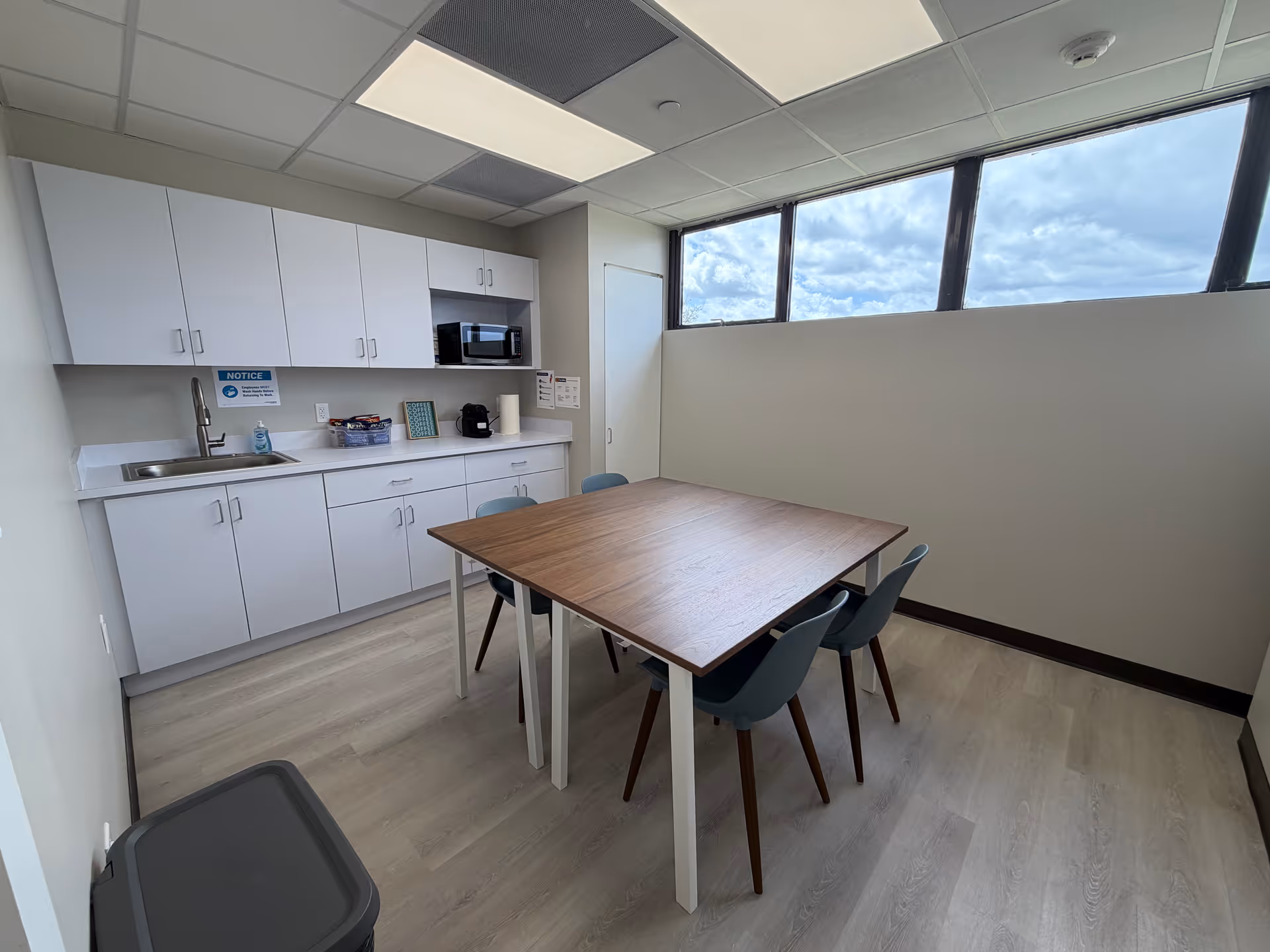 Modern kitchenette with white cabinets, sink, microwave, and a wood dining table with blue chairs.