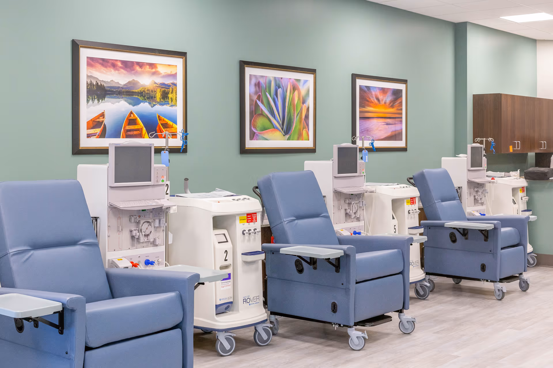 Row of blue recliners with dialysis machines along a green wall interior.