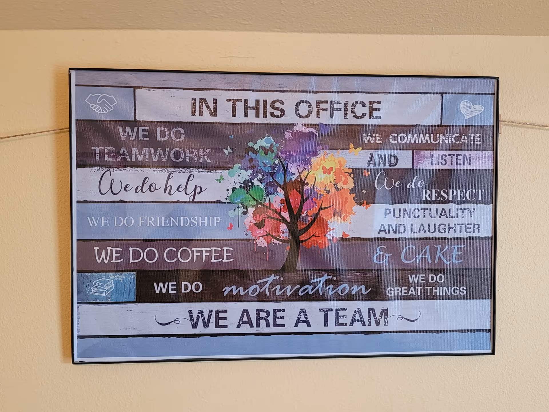 Framed colorful sign with inspirational phrases hangs on a yellow interior wall.