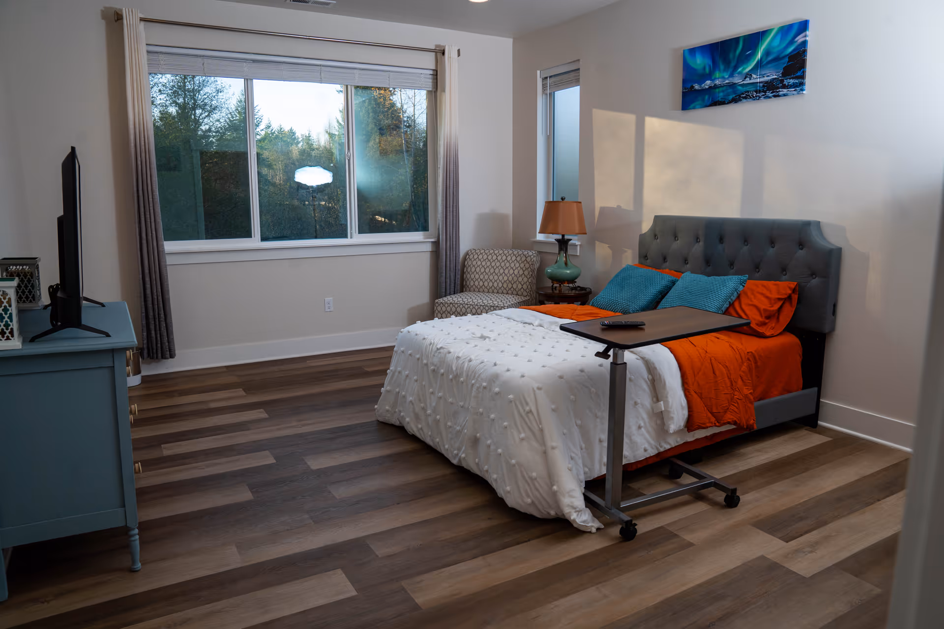 A furnished bedroom in a senior living facility with bed, dresser, and window.