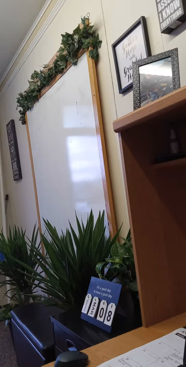 Interior office-like area with a whiteboard, potted plants, framed art, and a desk.