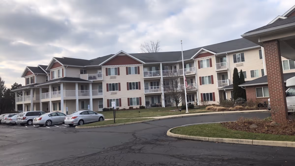 Exterior view of a multi-wing senior living facility with a parking lot and cars.