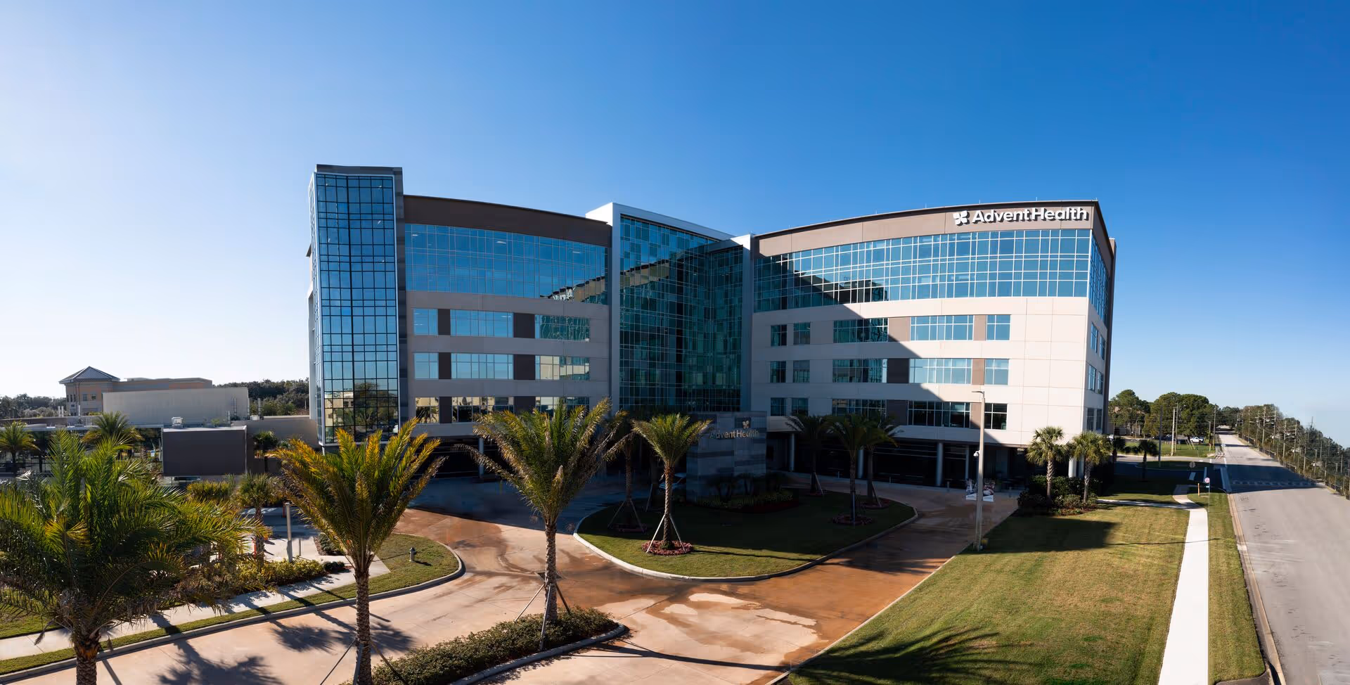 Exterior view of AdventHealth Hospice building with glass facade and palm-lined entrance.