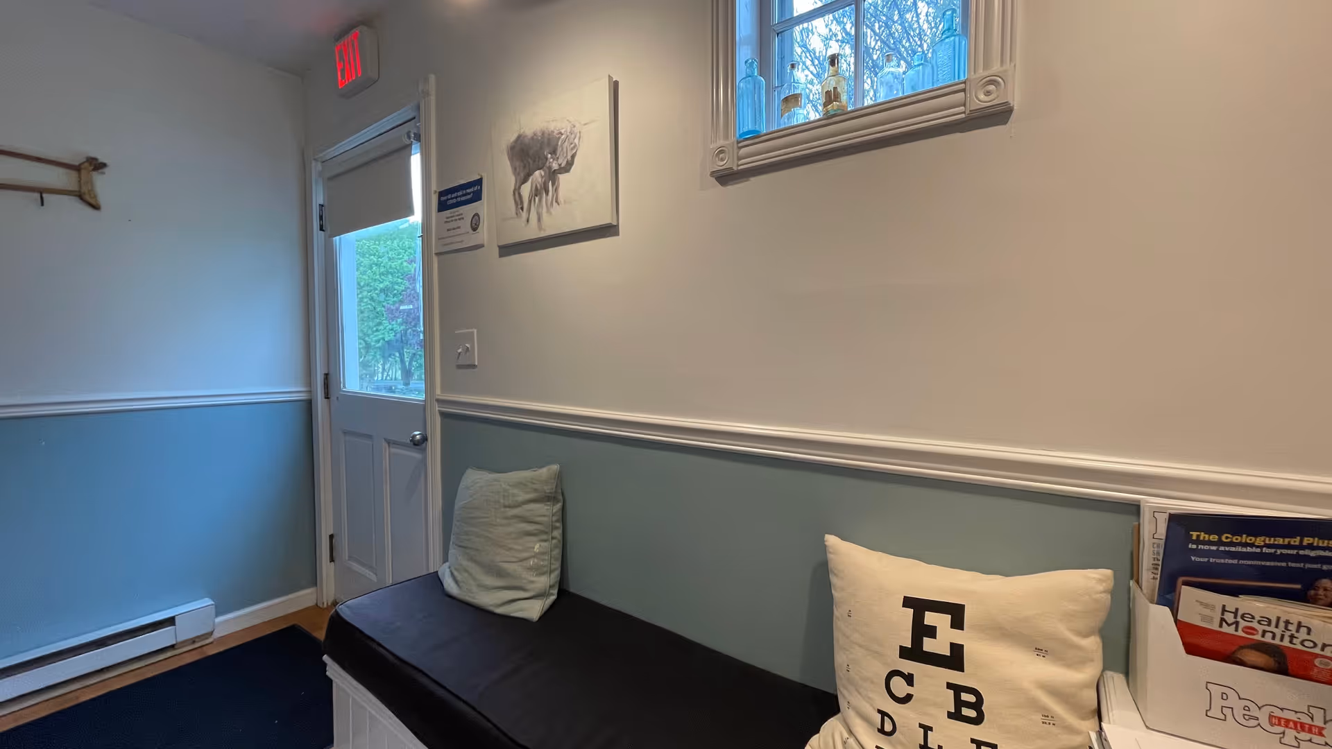 Small waiting area with a cushioned bench, wall paneling, exit door, and magazine rack.