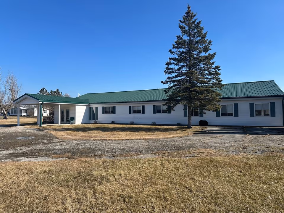 Gates AFC facility exterior with white siding, green metal roof, and a tall tree in front.