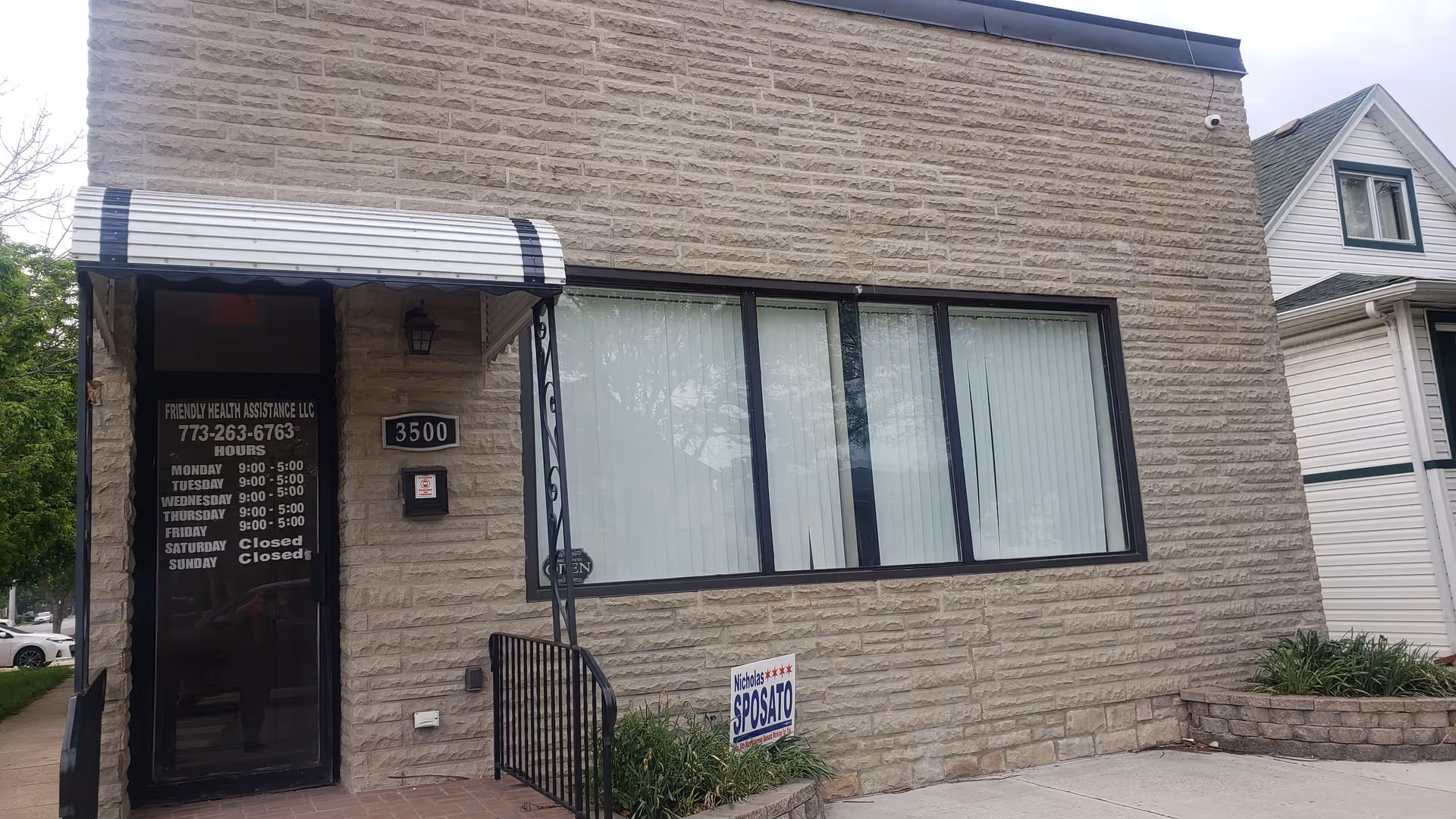 Exterior of a beige brick building with a glass front door, large window, and striped awning.