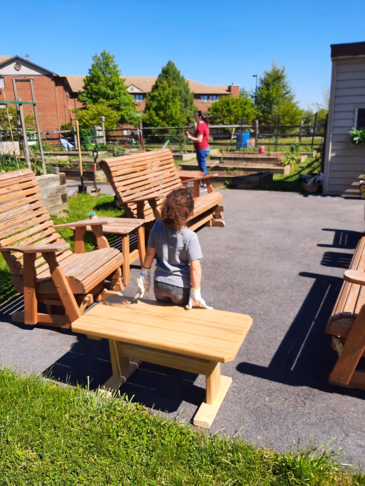 Outdoor courtyard with wooden chairs and a person in gloves tending garden area.