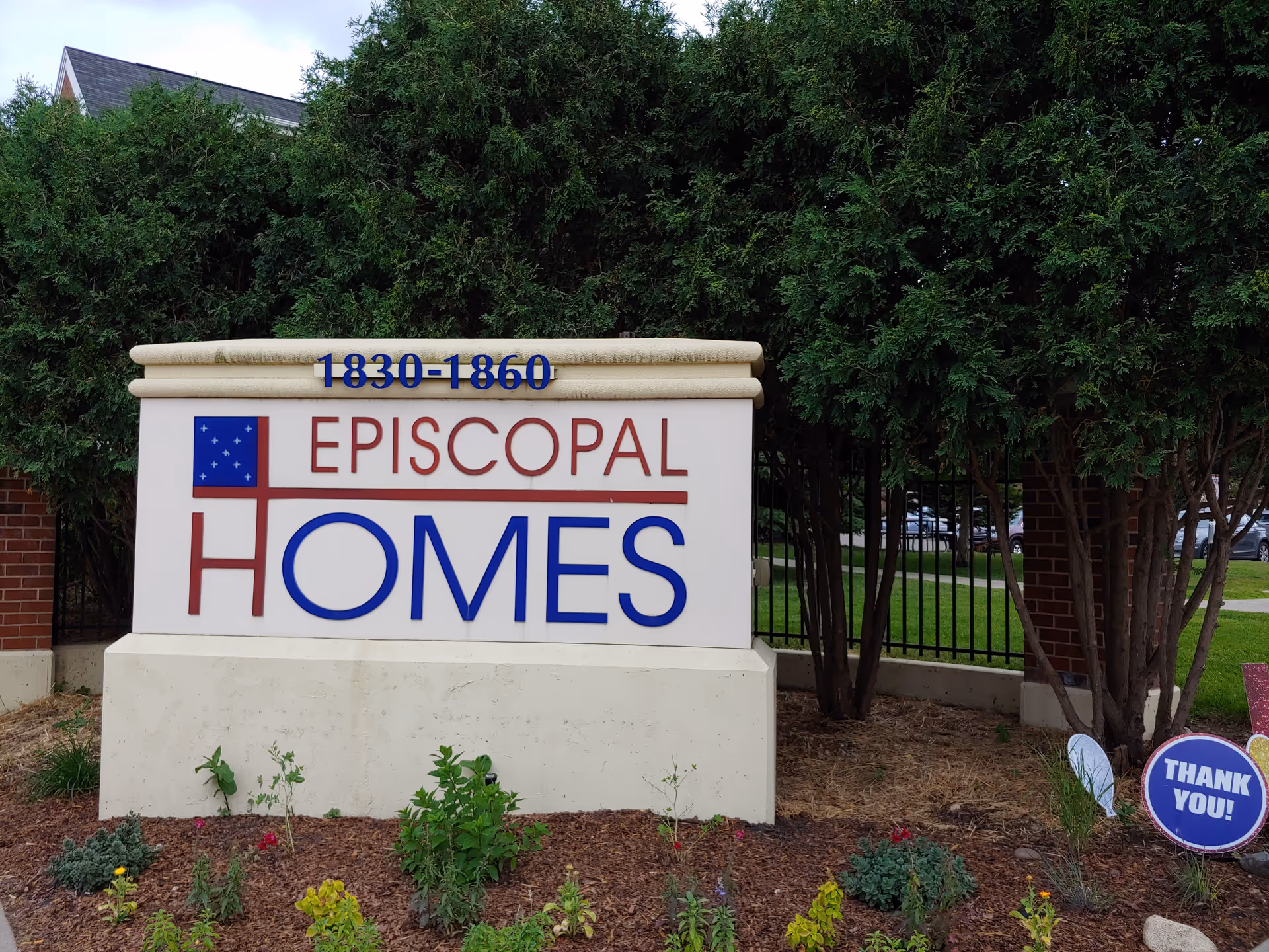 Entrance sign for The Gardens at Episcopal Homes with landscaping and trees.
