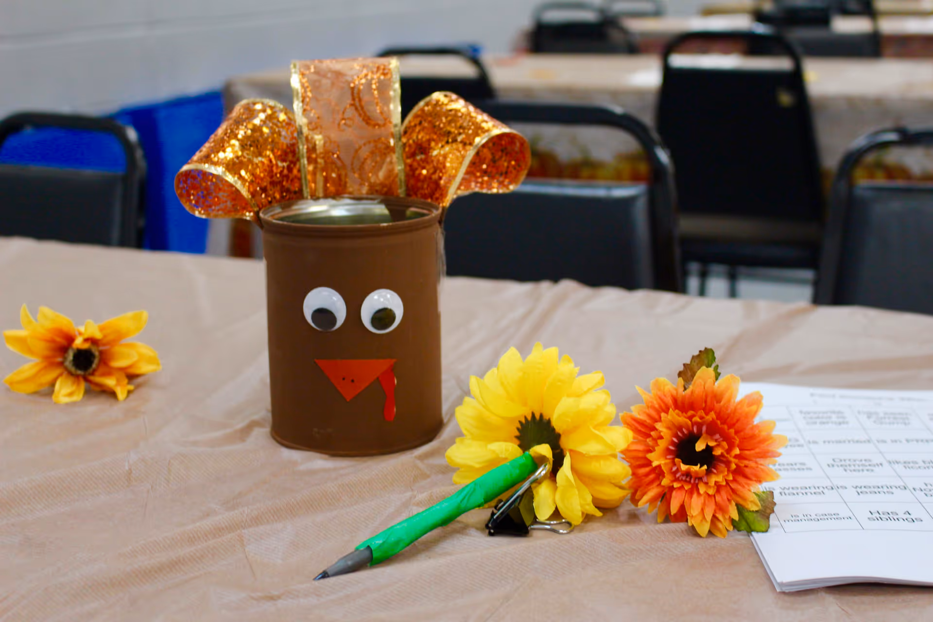 Table with a decorated painted tin can centerpiece, ribbons, flowers, and papers.