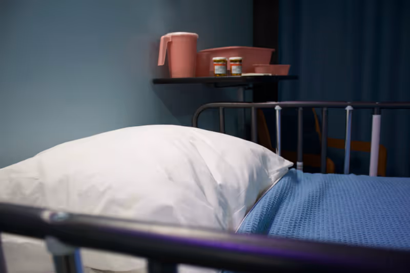 Hospital bed with white pillow and blue sheets in a patient room.