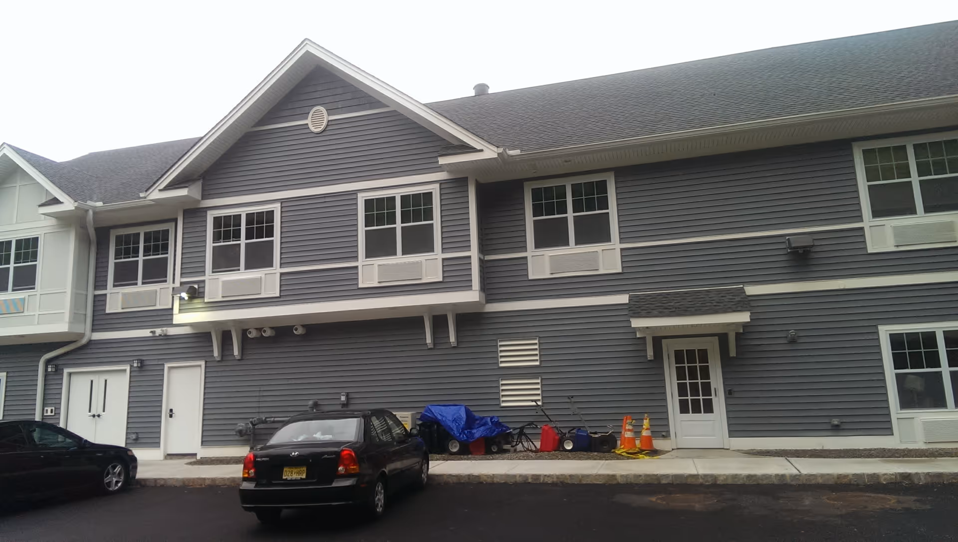 Two-story gray senior living building with windows, doors, and a parked car in front.