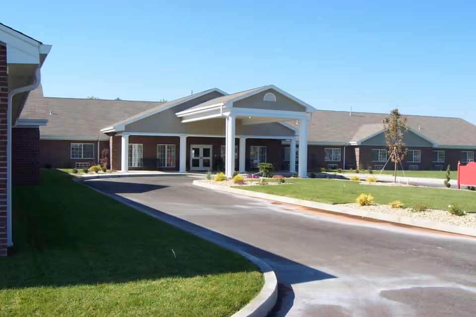 Exterior view of Covered Bridge Health Campus showing a single-story building with a covered entrance supported by white columns, surrounded by a well-maintained lawn and landscaping under a clear blue sky.