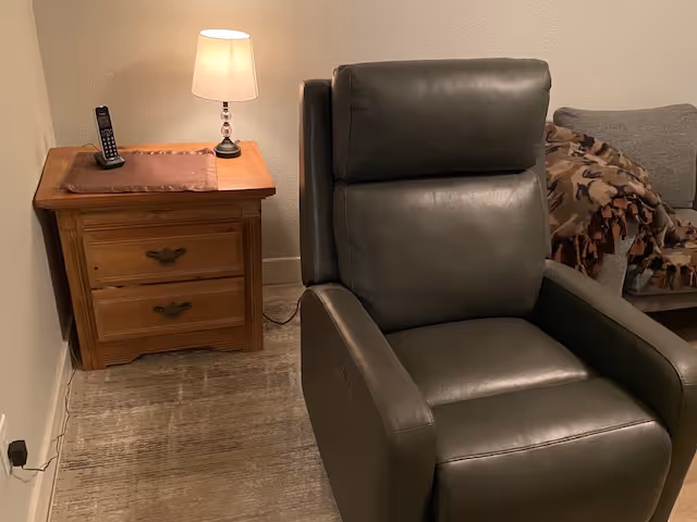 Leather recliner chair with a wooden nightstand and lamp in a cozy, residential living area.