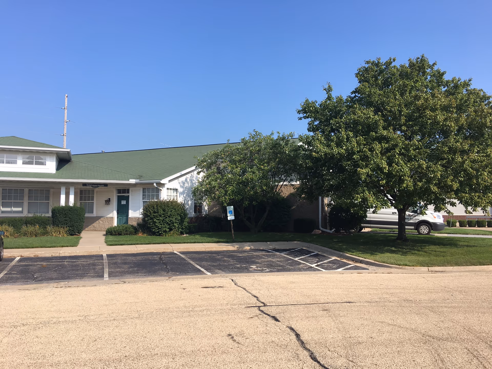 Exterior view of Total Home Health building with green roof, parking lot, and trees.