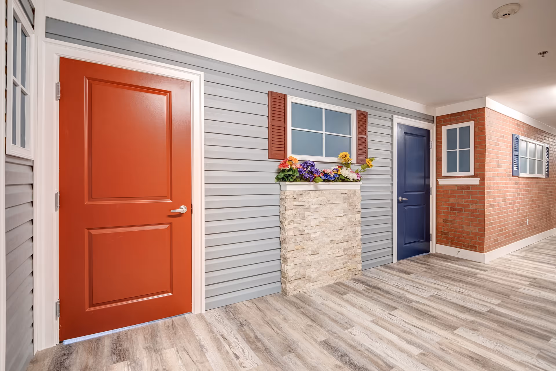 Colorful interior corridor with red and blue doors, faux brick wall, and flower planter.