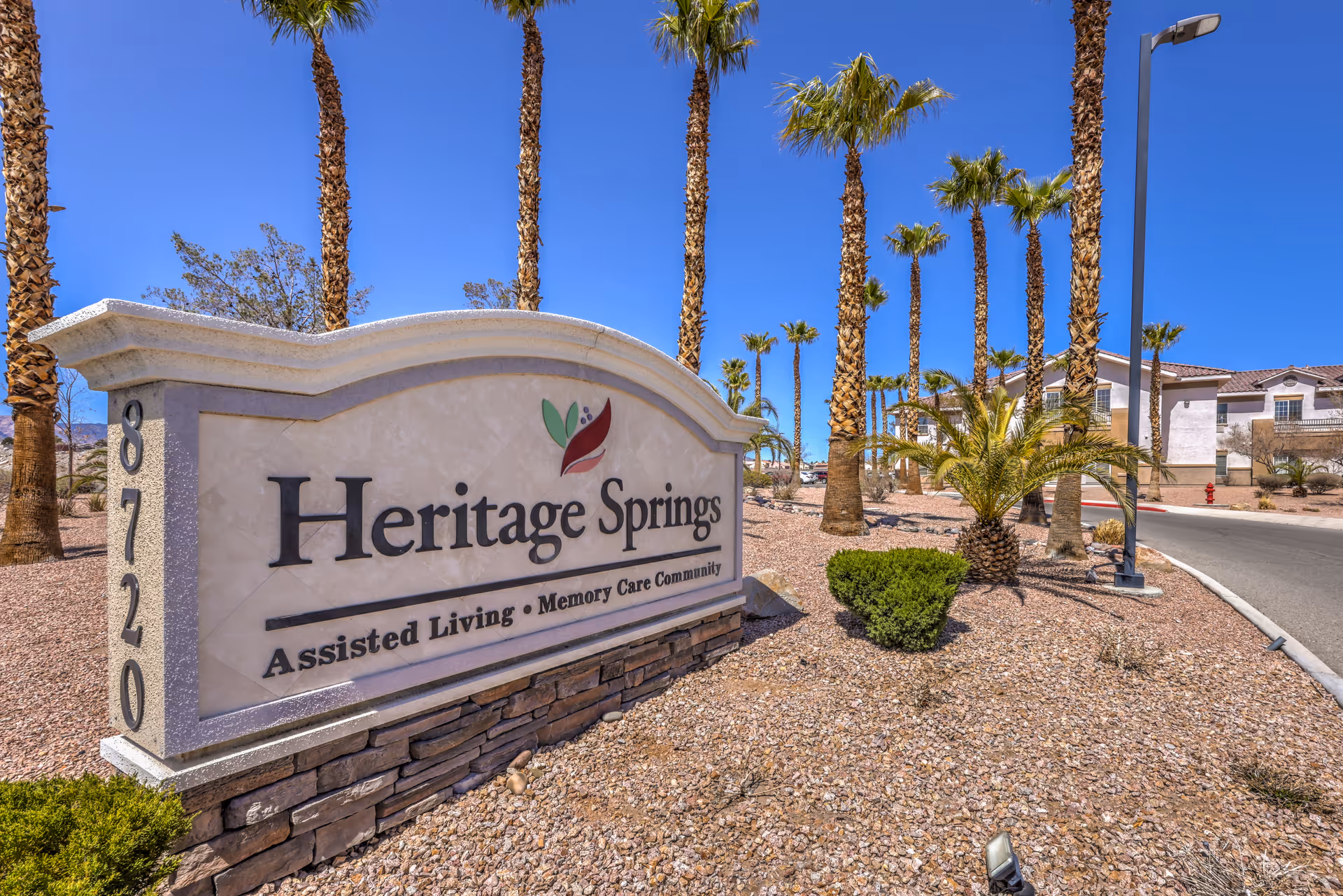 Heritage Springs entrance sign with palm trees and desert landscaping in a sunny exterior setting.