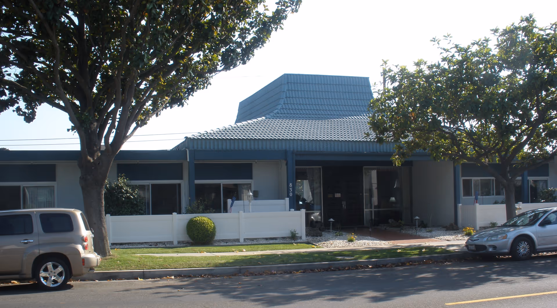 Front view of Country Oaks Care Center with trees, a blue roof, and parked cars.