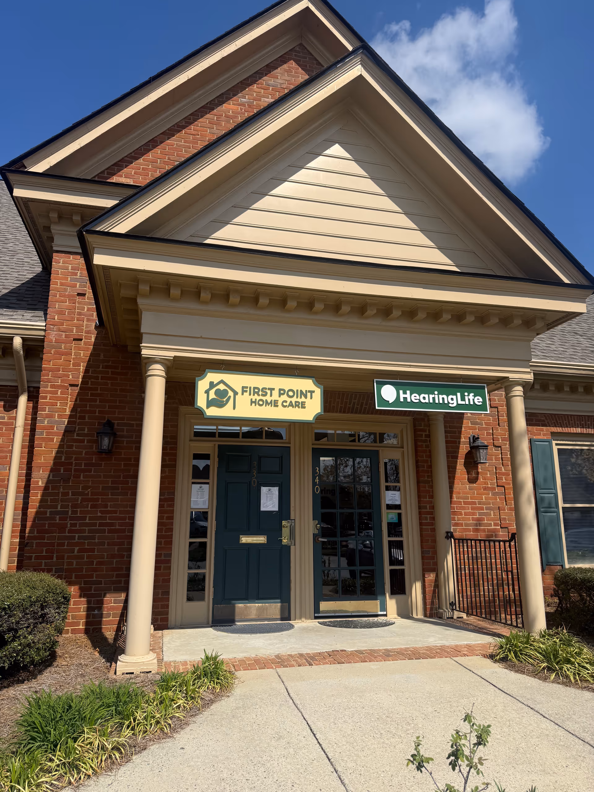 Front entrance of a brick care facility with First Point Home Care and HearingLife signs.