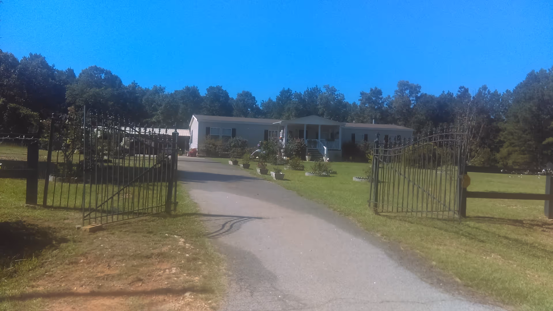 Gated gravel driveway leads to a single-story senior living facility with manicured lawn.