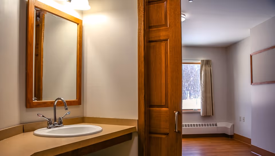 Bathroom vanity with sink and mirror, open door to a sunlit room.
