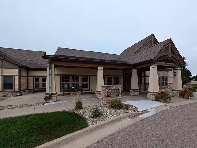 Exterior view of a beige, stone-accented senior care facility entrance with a covered portico.
