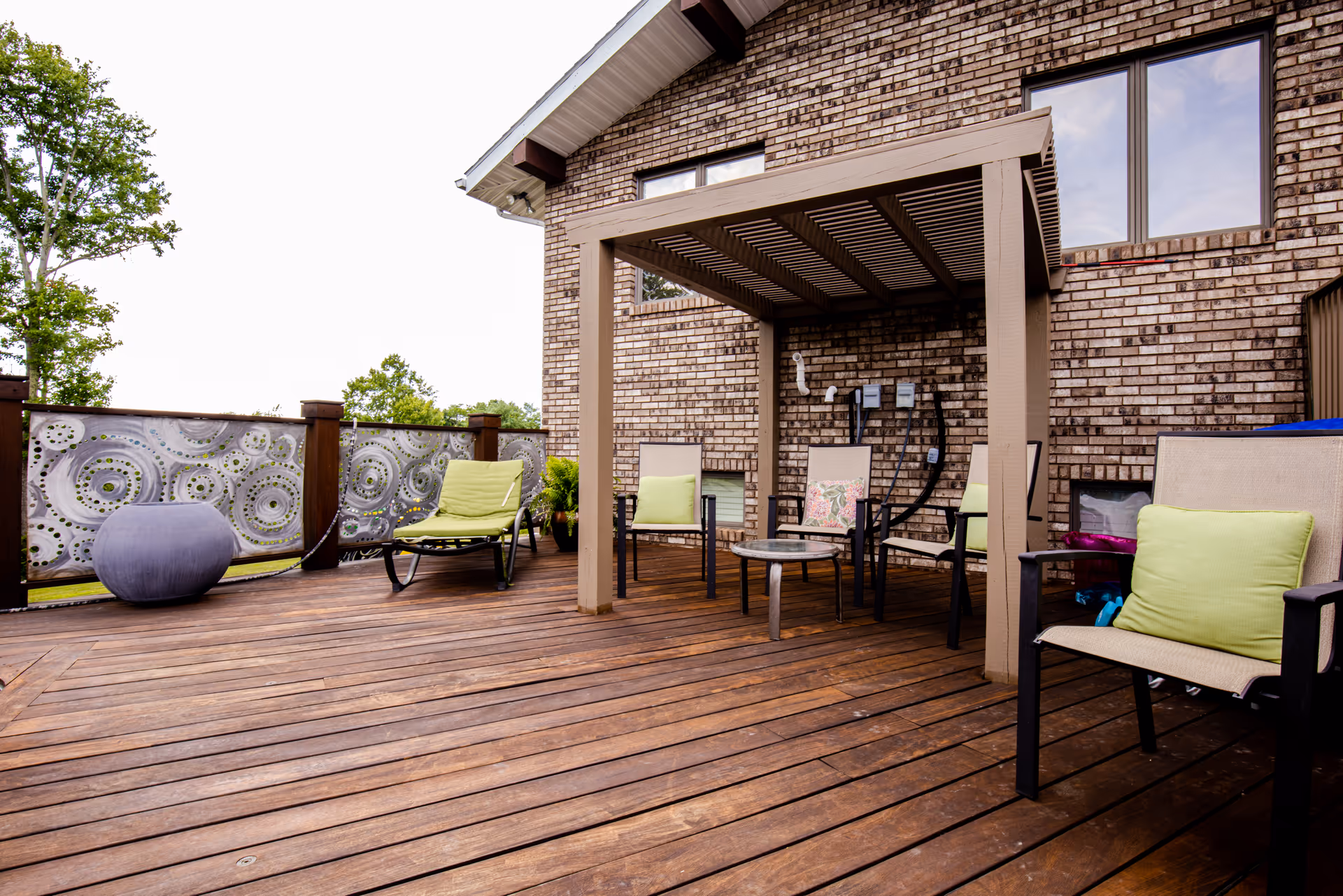 Brick home with a wooden deck, pergola, and outdoor seating area with lime-green cushions.