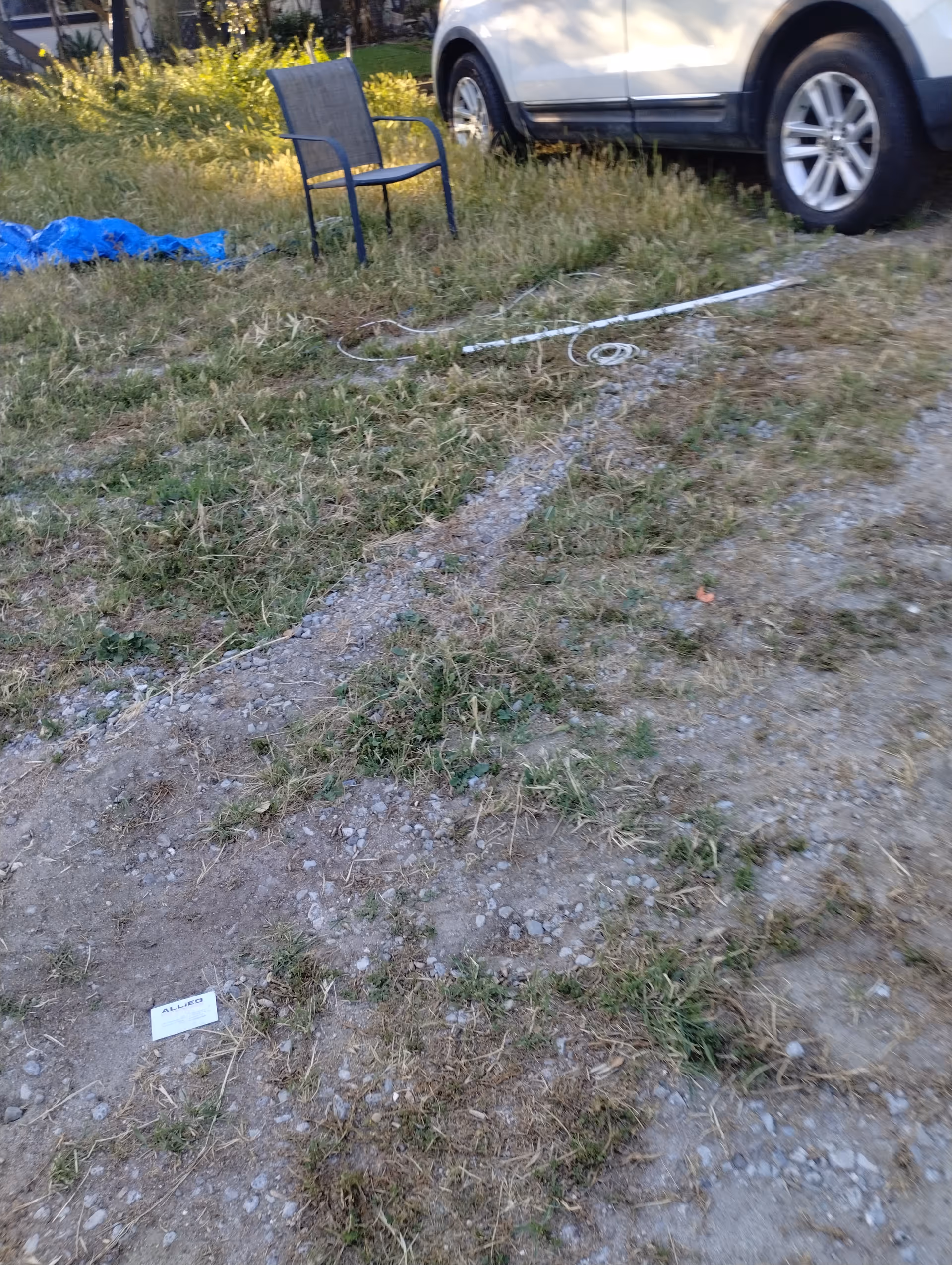 Outdoor area with a lone chair on grass, a parked car, and tangled cords.