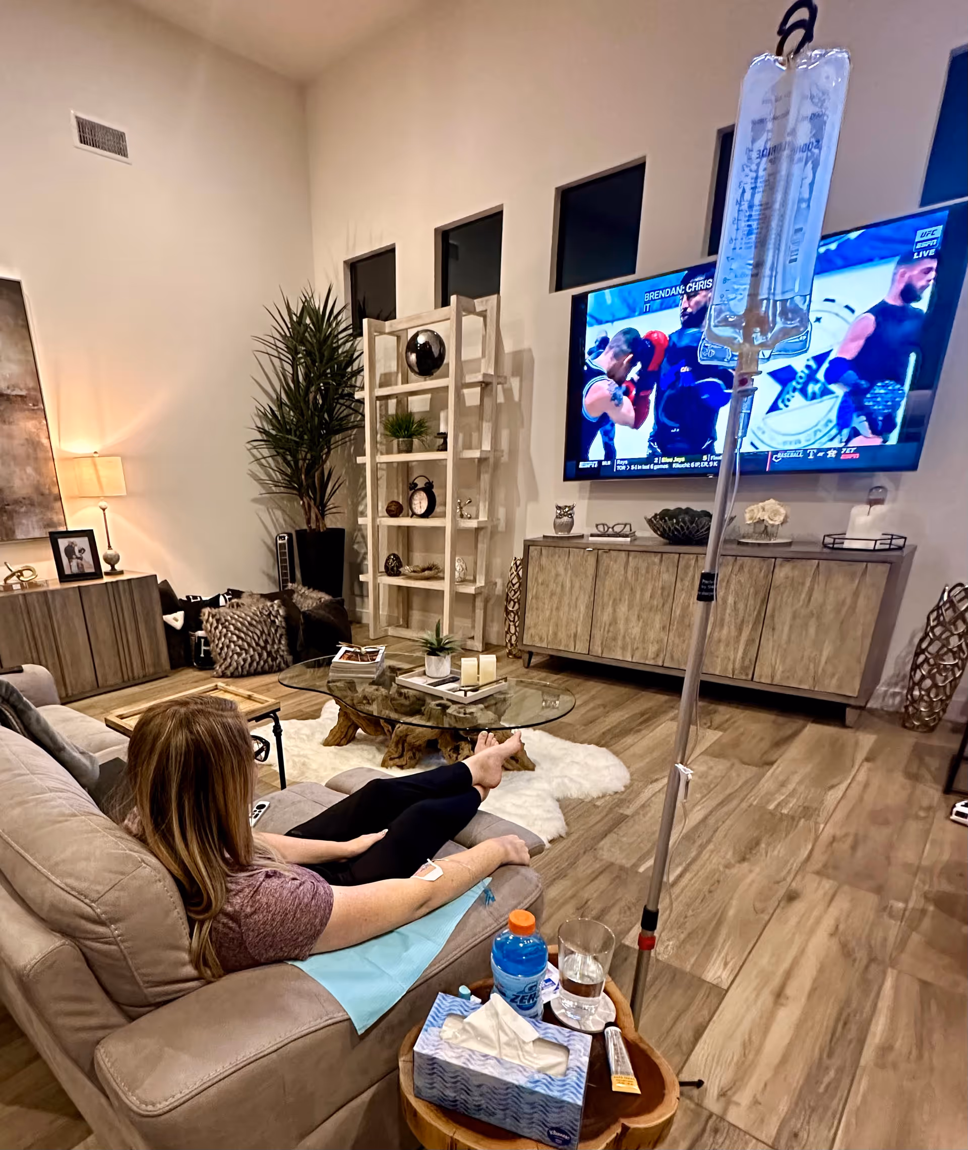 A living room scene with a person on a sofa watching TV and an IV drip.