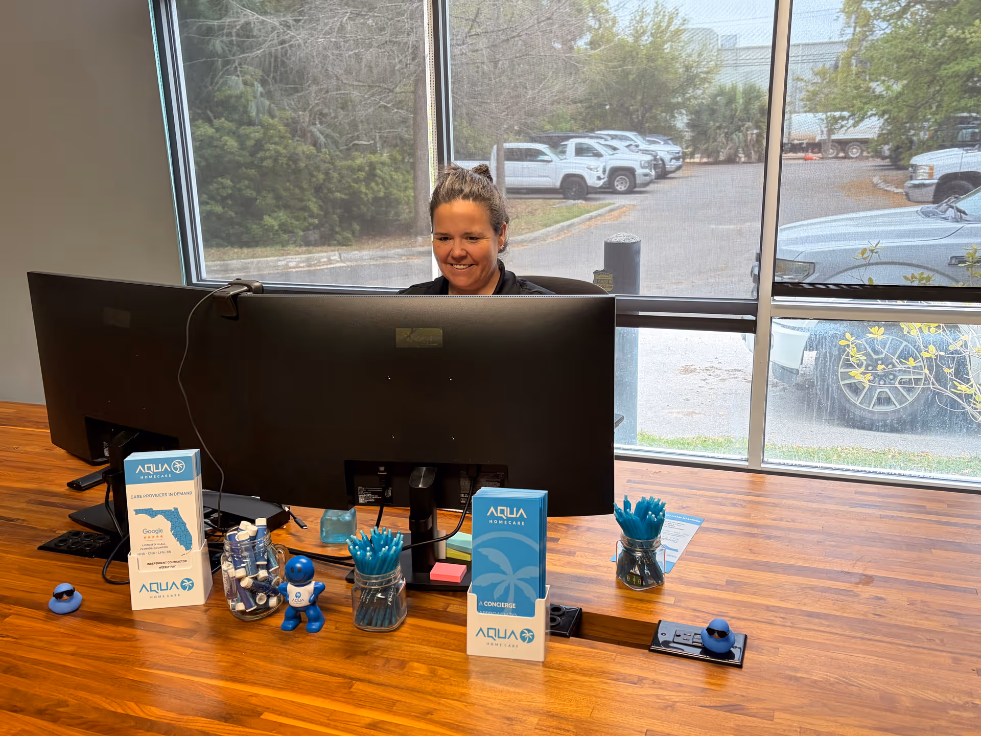 Reception area with a smiling staff member behind a curved desk and monitors.