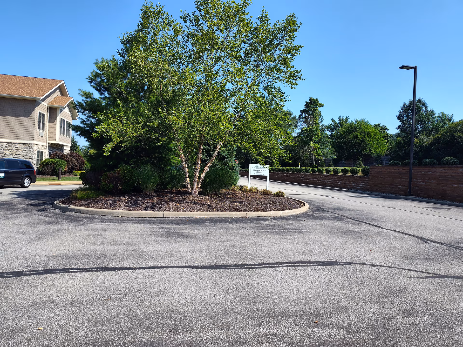 Curved driveway circles a landscaped median with trees in front of a beige senior living building.