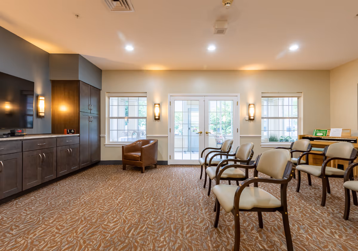 Interior senior living common area with chairs, cabinets, and glass doors.