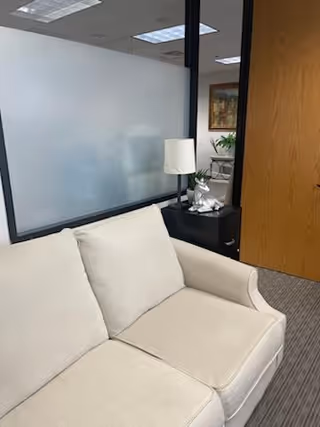 Beige sofa in a small office-like waiting area with frosted glass partition and lamp.