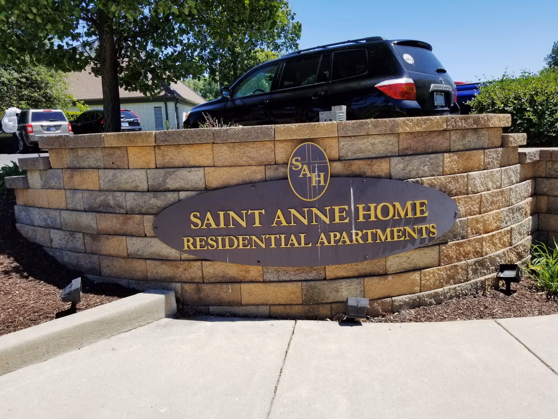 Stone wall with Saint Anne Home sign and parked cars at the entrance