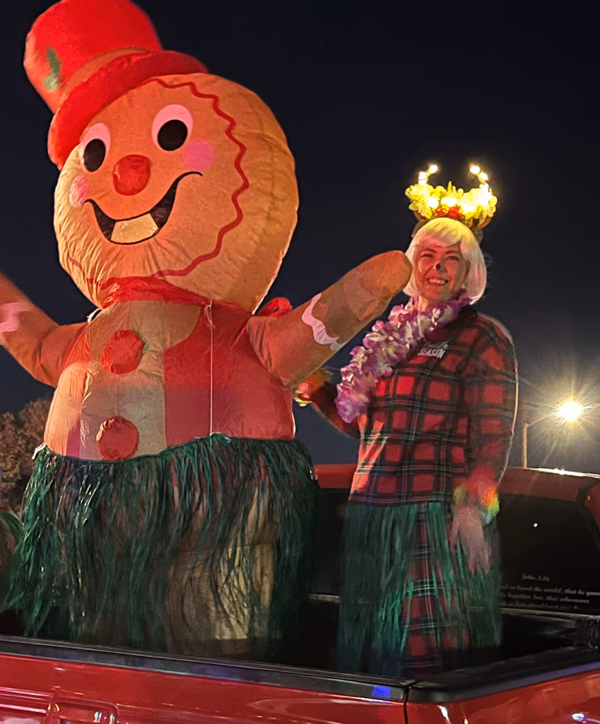 Person in plaid shirt with lei beside a giant inflatable snowman on a truck at night.