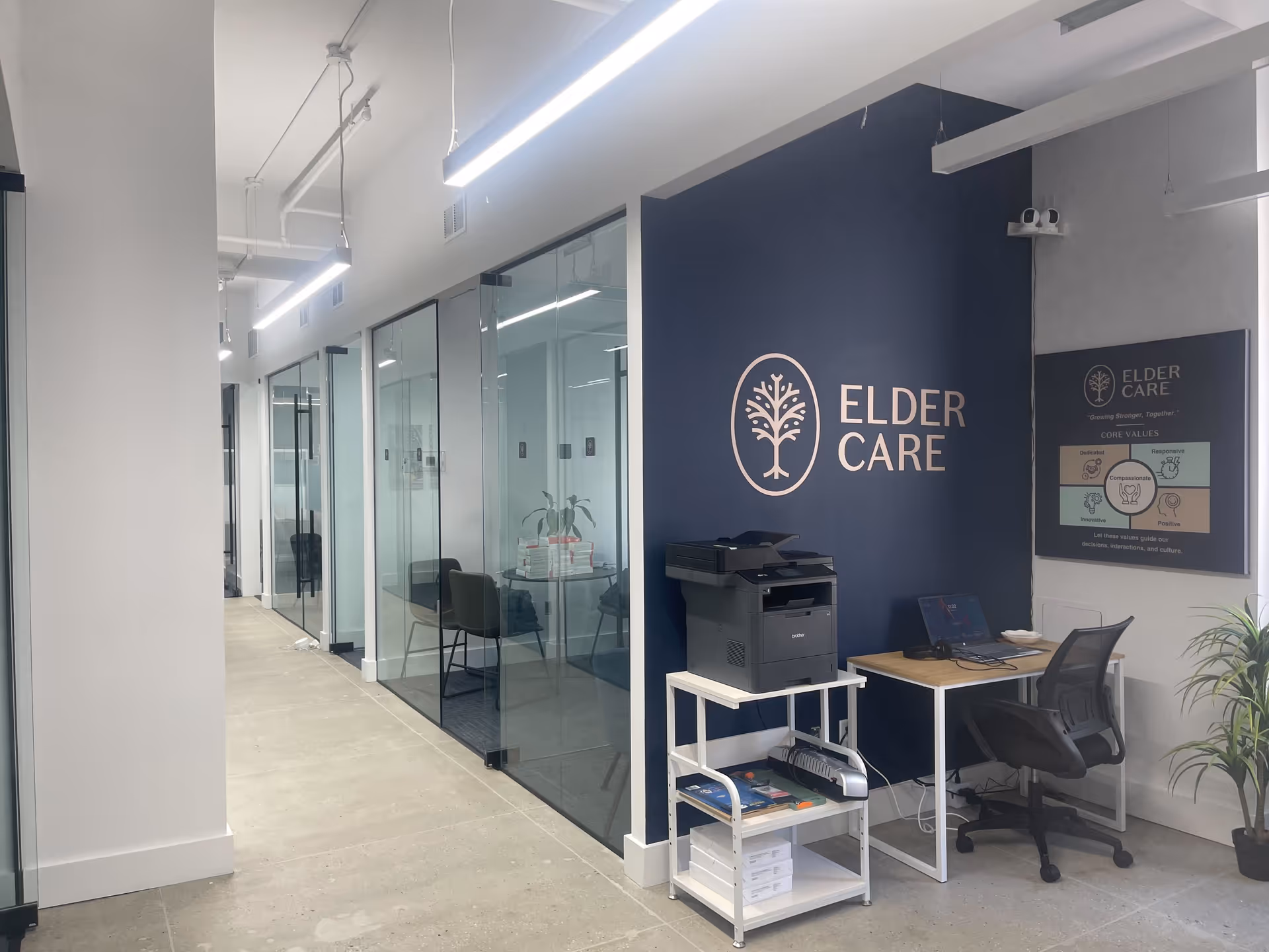Interior hallway of Elder Care facility with glass-walled offices and a workstation.