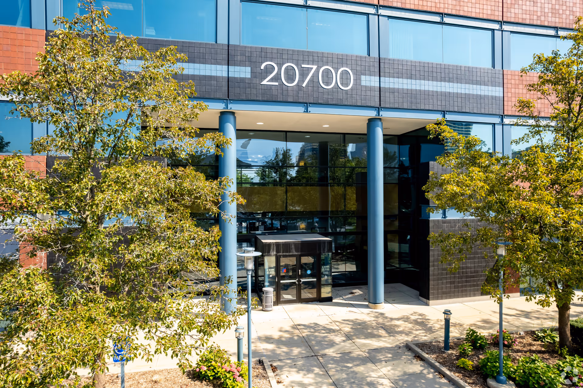Modern glass-front building entrance framed by blue columns and trees.
