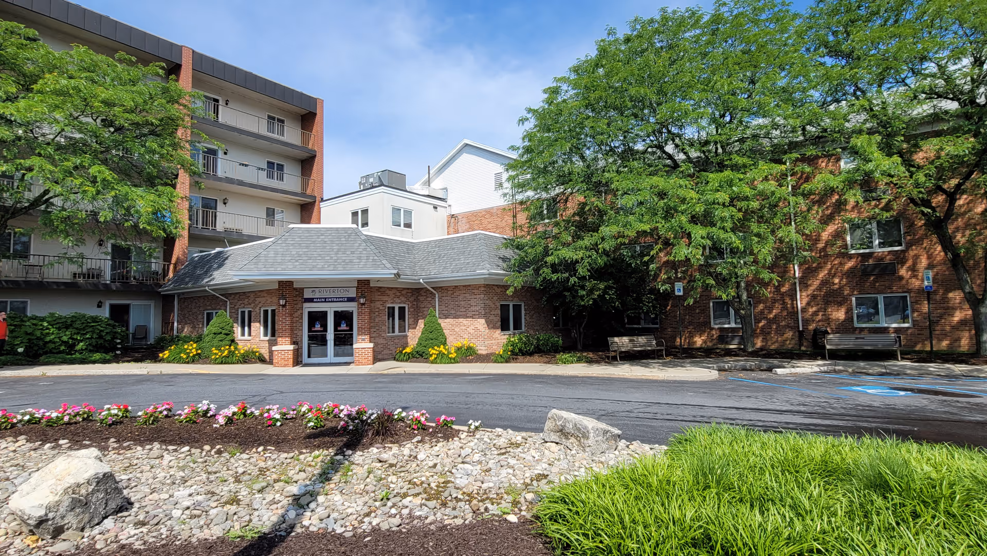 Brick building with a covered entrance, landscaping, and trees in front of Riverton Enhanced Senior Living.