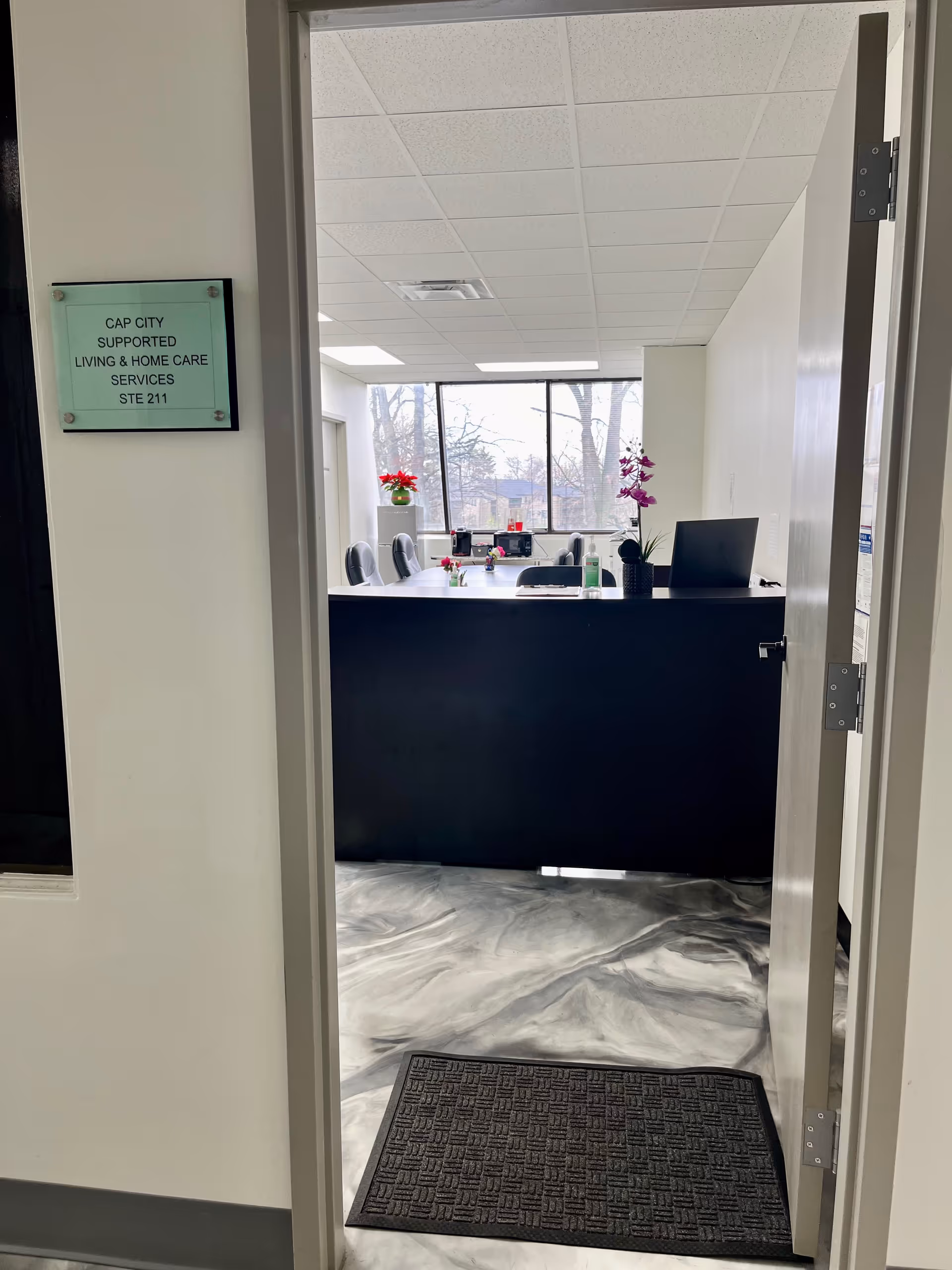 Interior reception area with a dark front desk, chairs, plants, and a large window.