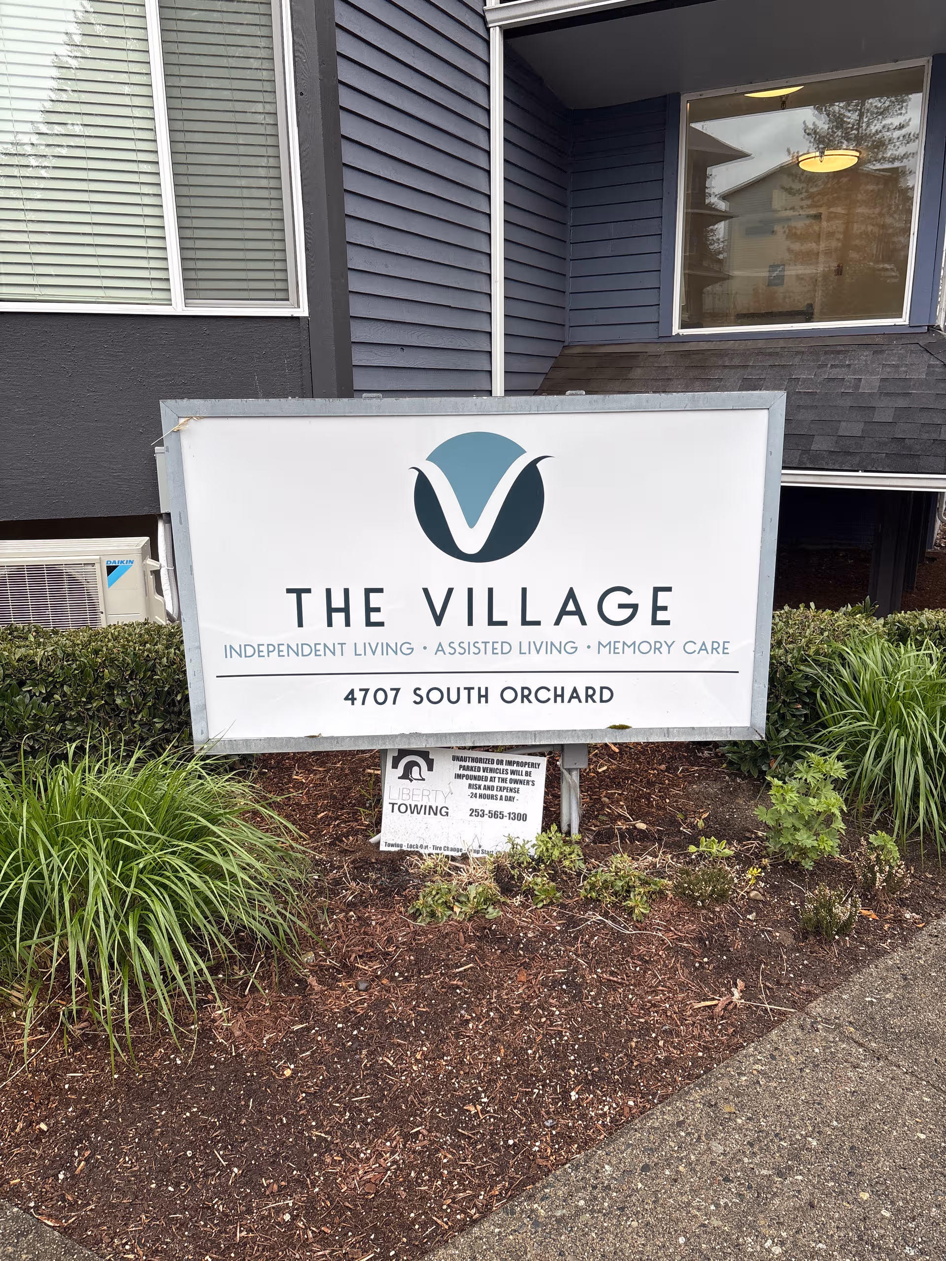 Exterior view of The Village Senior Living sign outside a blue-gray building.