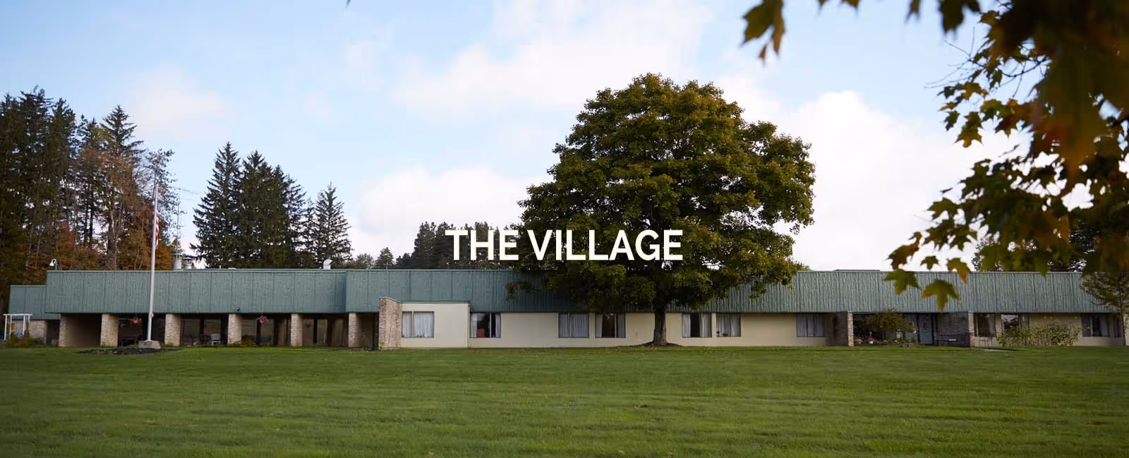 Single-story building with teal roof and green lawn, THE VILLAGE sign visible.