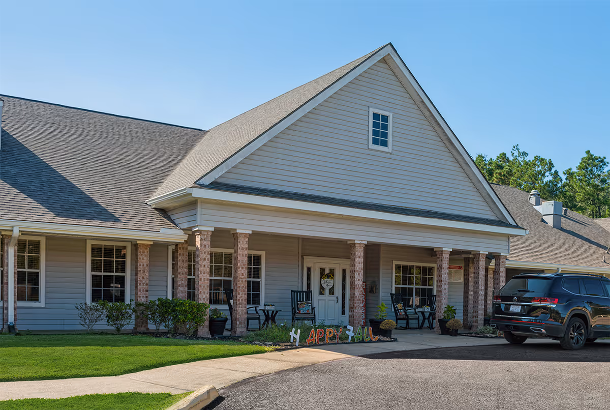 Front view of Sabine Place senior living facility with porch seating and a parked SUV.