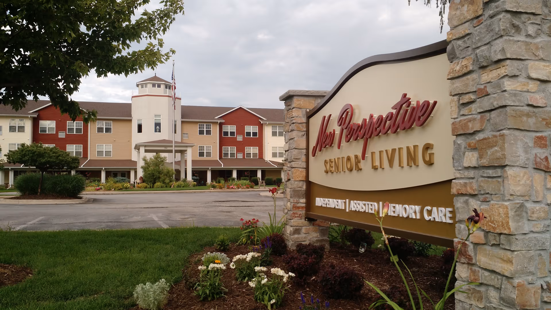 Exterior view of New Perspective Senior Living facility with a large stone sign and landscaped entrance.