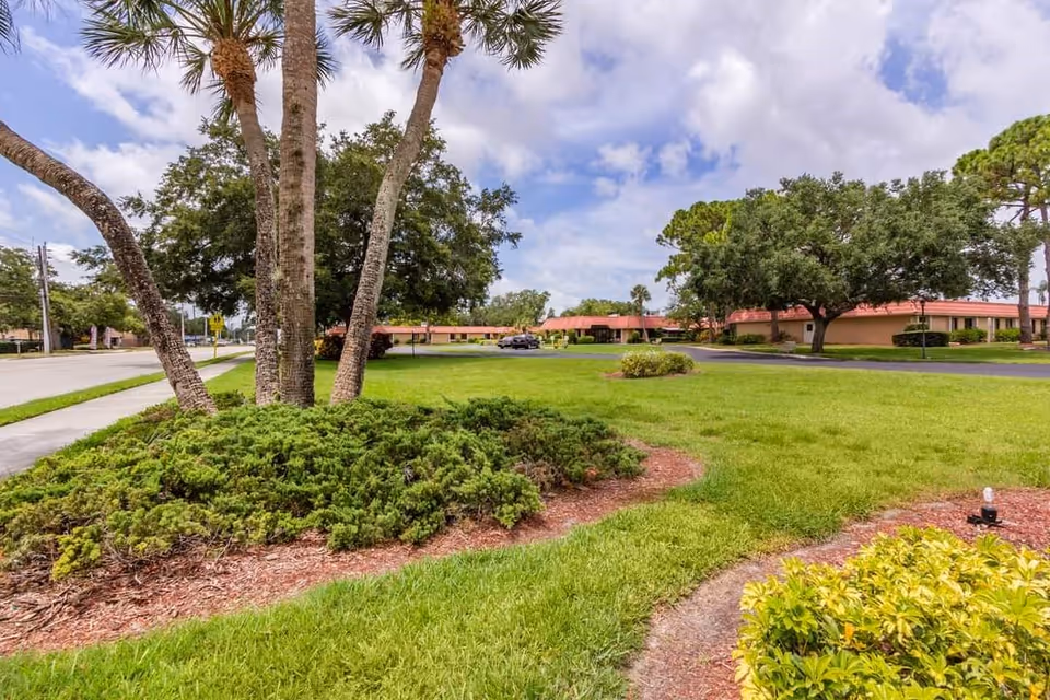 Lush landscaped exterior with palm trees and a single-story facility in the distance.